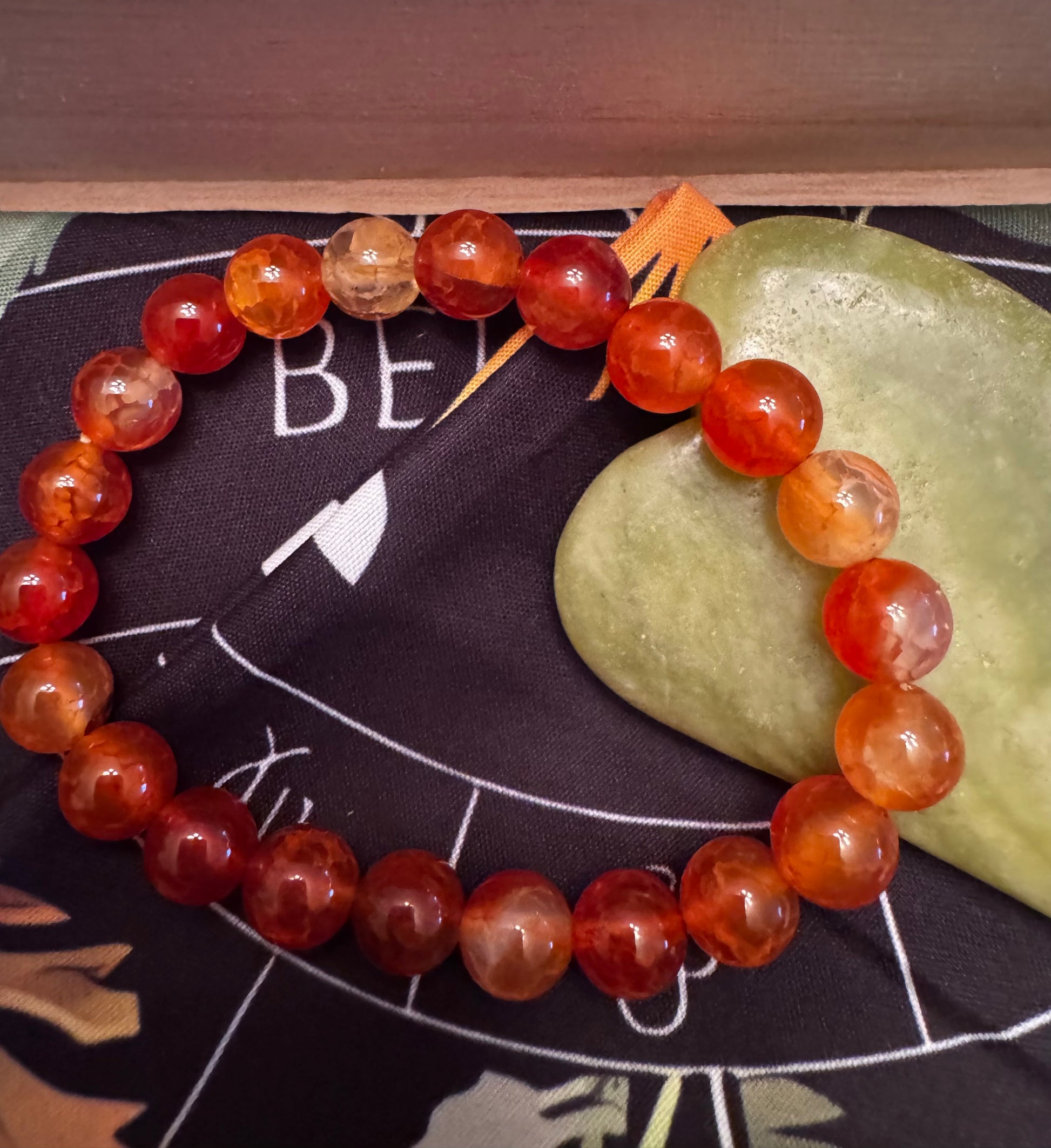 Red and orange beaded bracelet on a dark fabric with astrology symbols and green stone.
