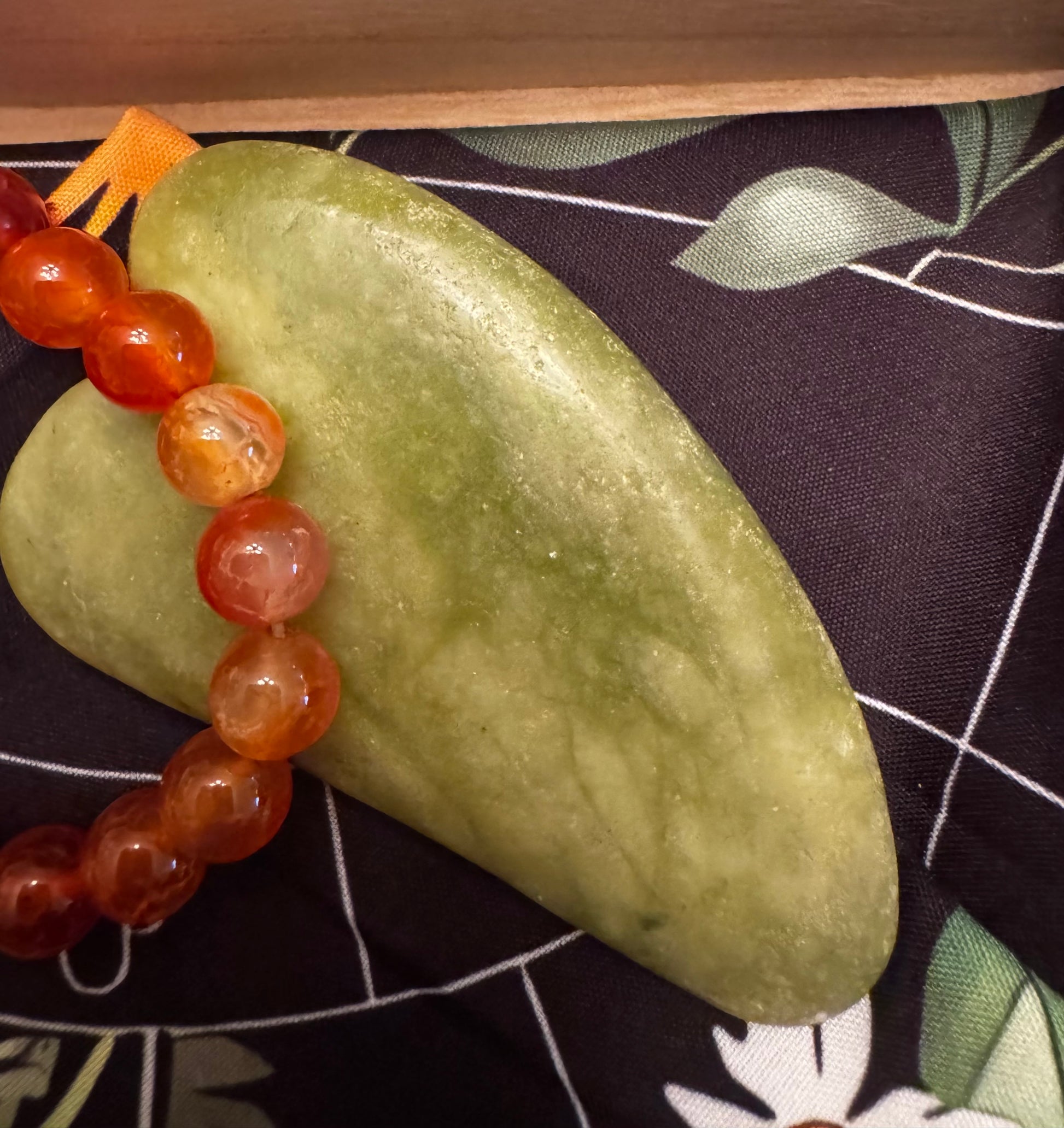 A jade heart with orange beads on a floral cloth.