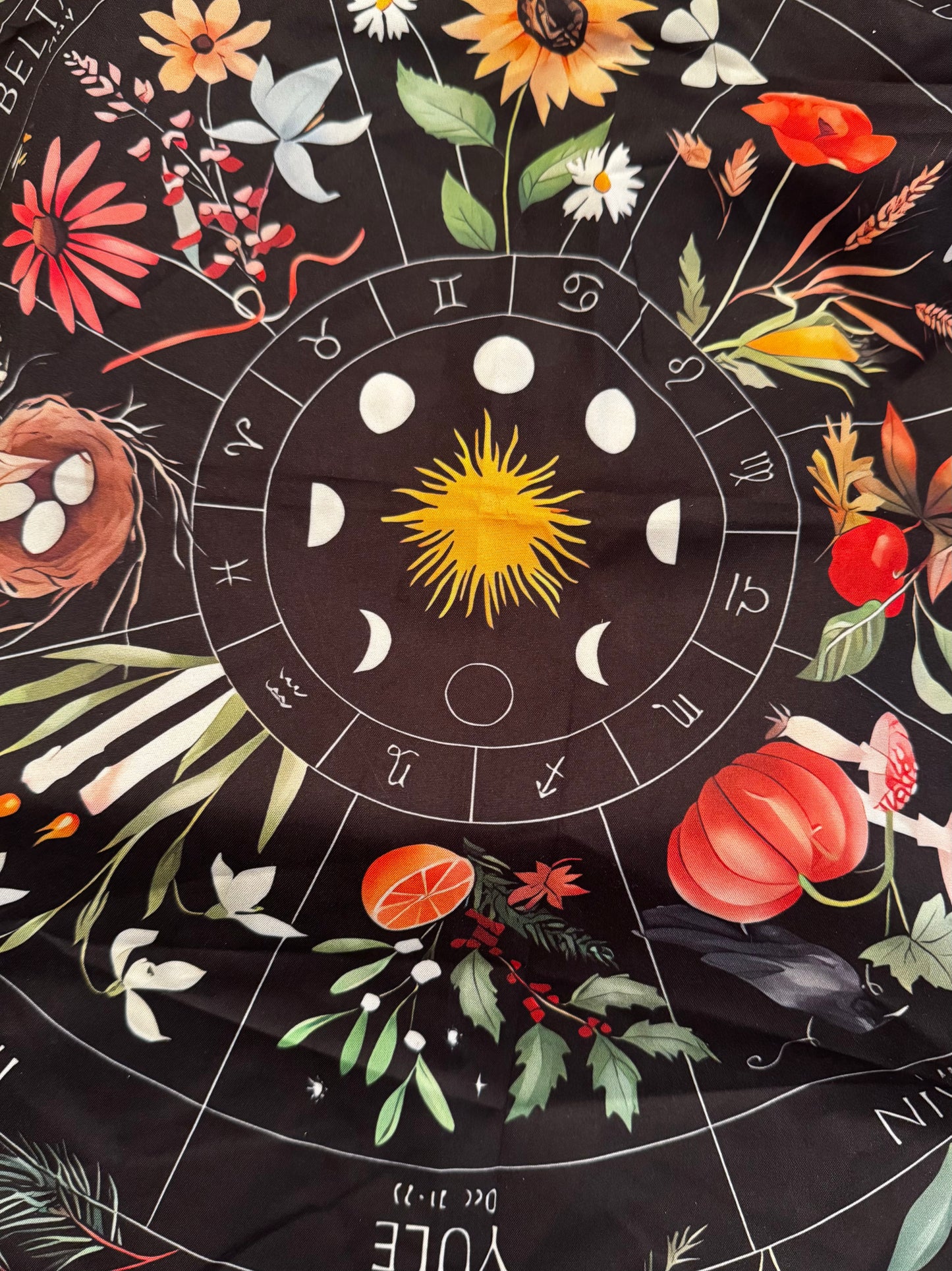 A black cloth featuring a zodiac wheel, moon phases, seasonal flowers, and other images.