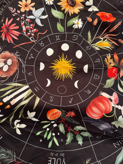 A black cloth featuring a zodiac wheel, moon phases, seasonal flowers, and other images.