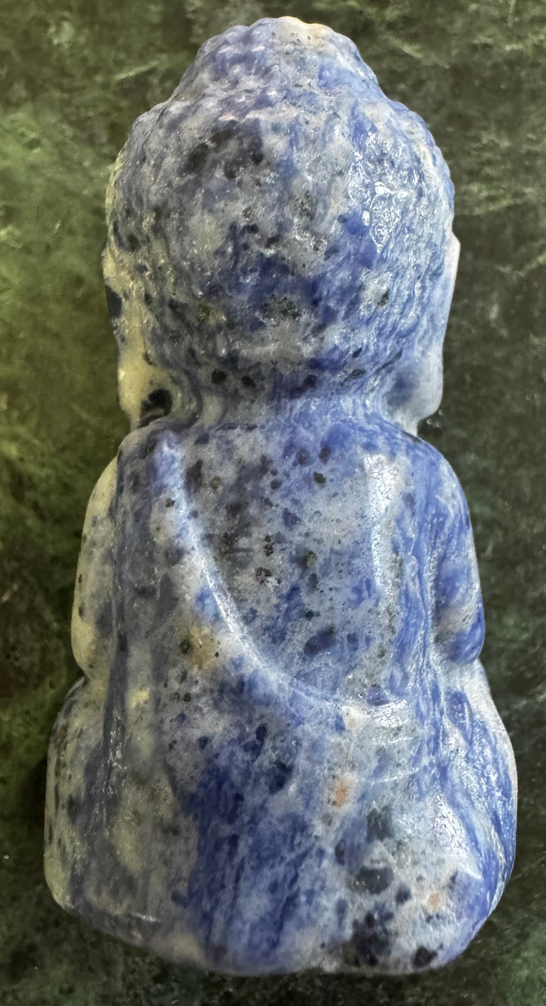 Close-up back view of a blue and white speckled stone Buddha figurine in a seated position.