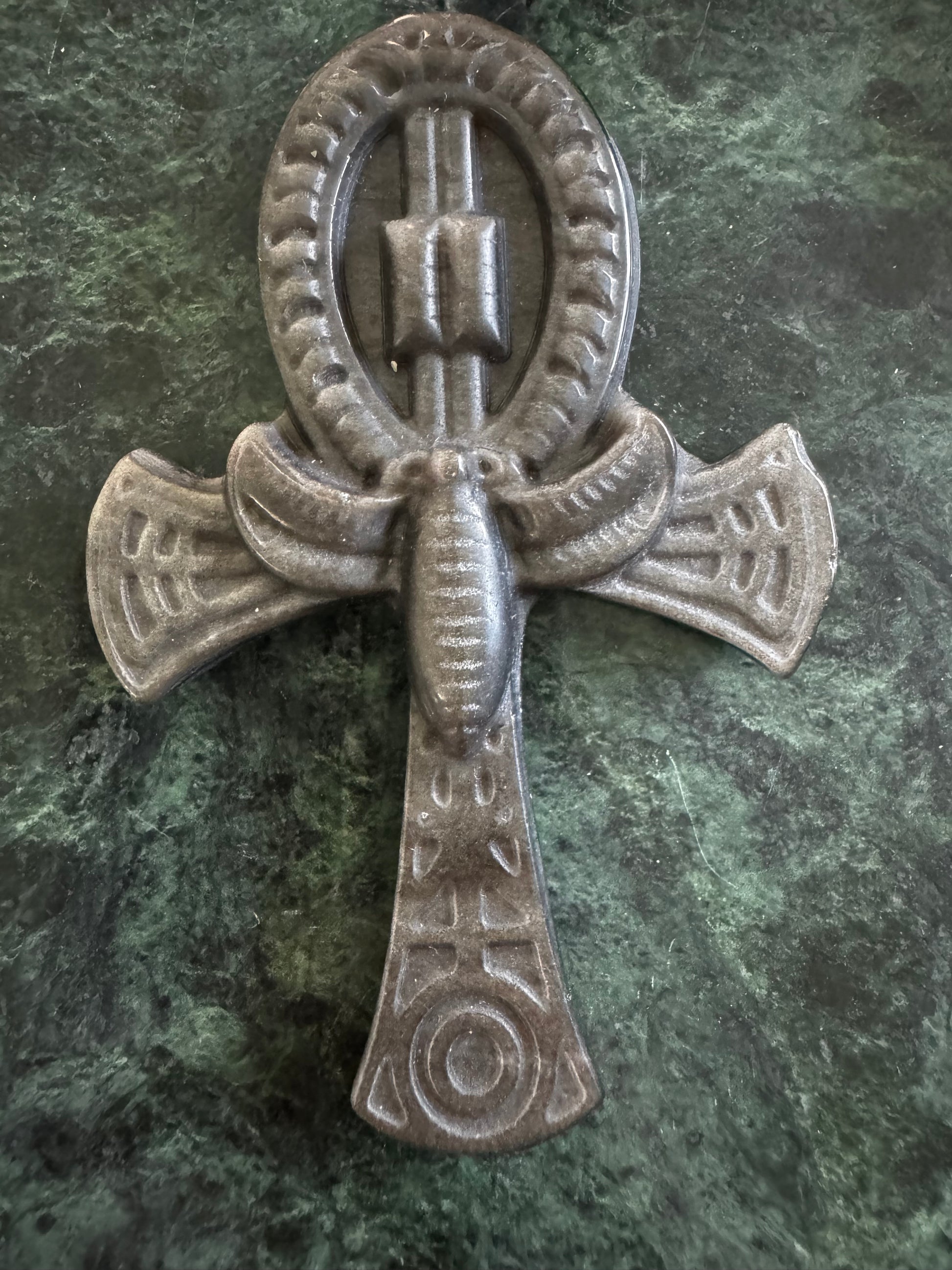 Stone Ankh with outstretched wings on a green marble surface.