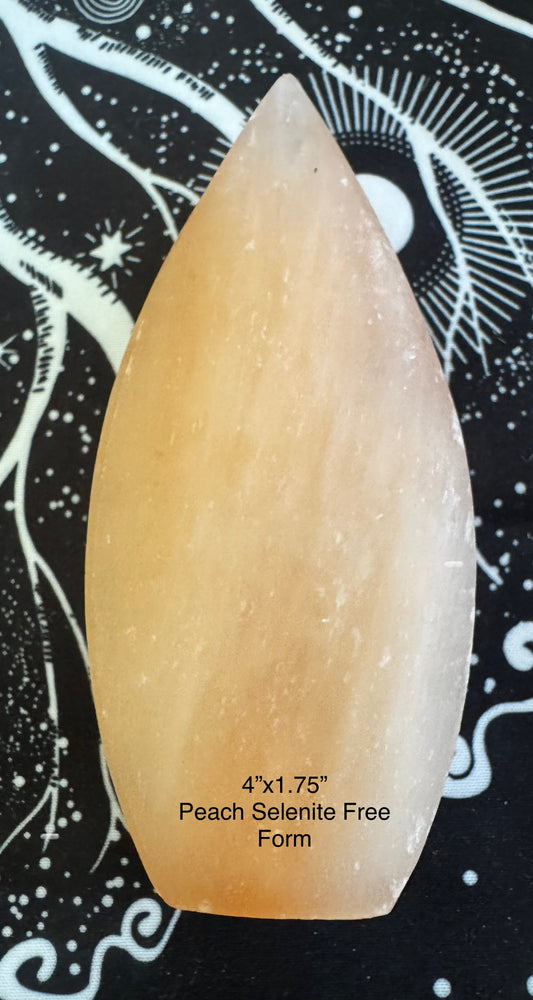 Peach selenite free form with a leaf shape on a black and white patterned surface.