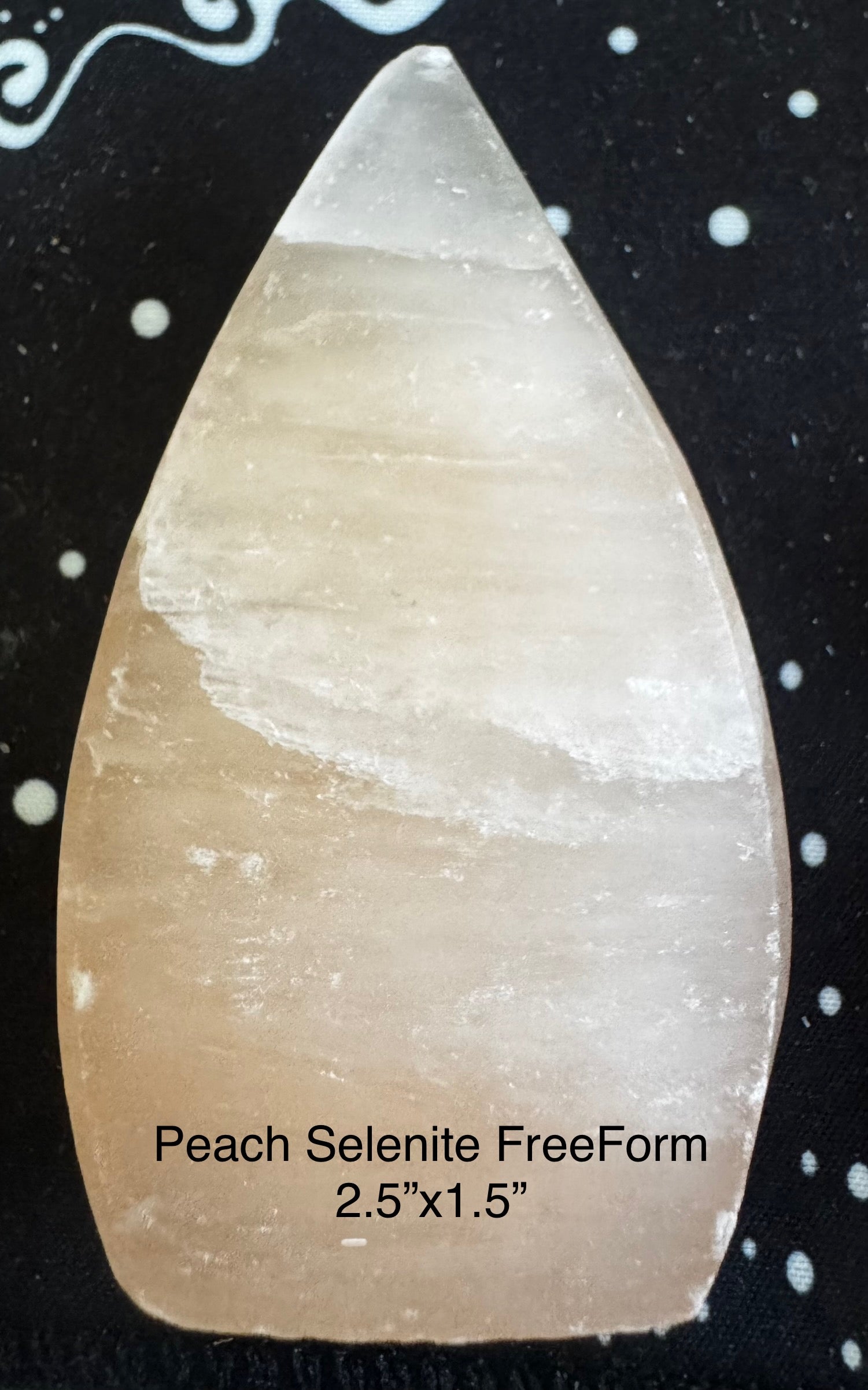 Peach selenite freeform on black fabric with white dots.