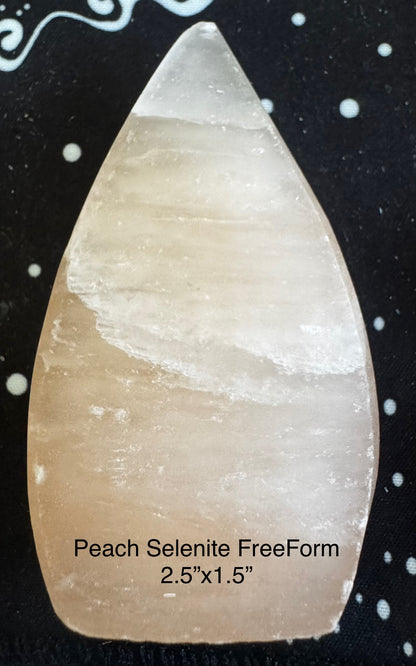 Peach selenite freeform on black fabric with white dots.