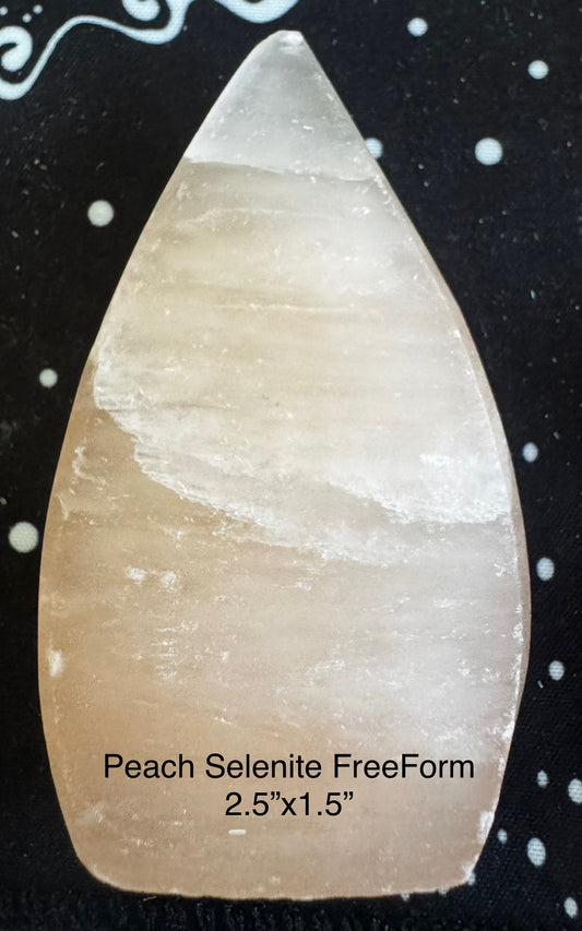 Peach selenite freeform on black fabric with white dots.