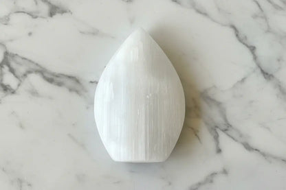 A white selenite crystal on a black and white patterned surface.