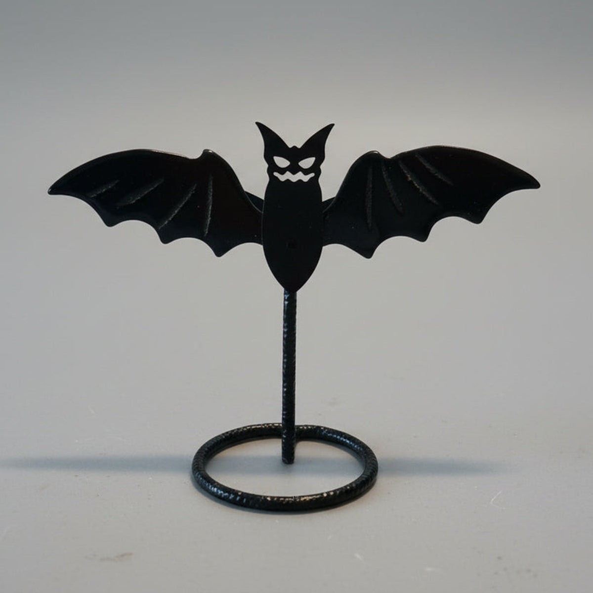 Black bat-shaped object on a stand against a neutral background