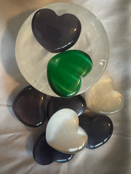 Polished, heart-shaped gemstones in black, green, and white colors arranged on a translucent plate over a wrinkled fabric.
