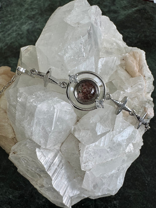 Silver bracelet with red stone and diamond accents, displayed on a white crystal.