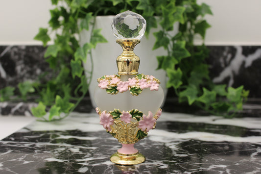 pink and green flowers on a gold tone mini frangrance bottle on a counter with ivy behind