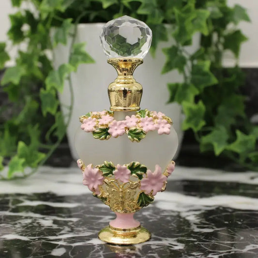 pink and green flowers on a gold tone mini frangrance bottle on a counter with ivy behind