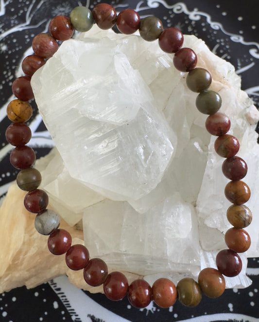 Picasso Jasper Quartz Beaded bracelet featuring shades of red, brown, and green, resting on a white crystal.