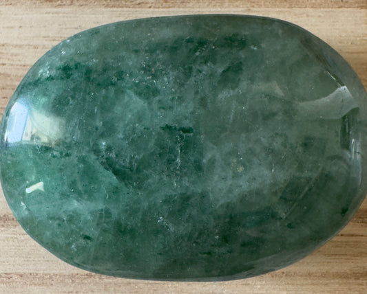 Polished green crystal stone on wood surface.
