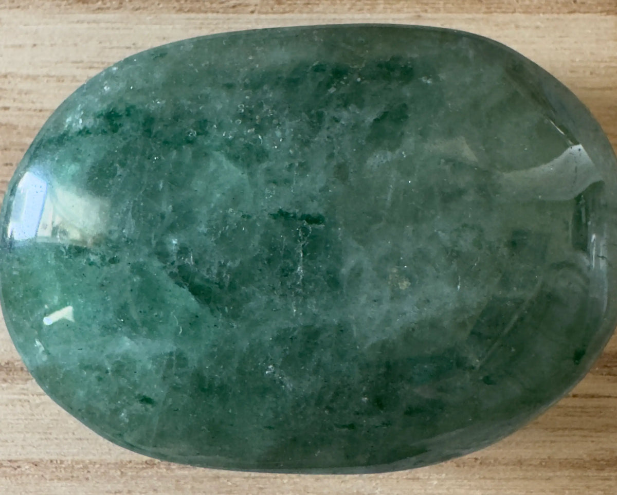 Polished green crystal stone on wood surface.