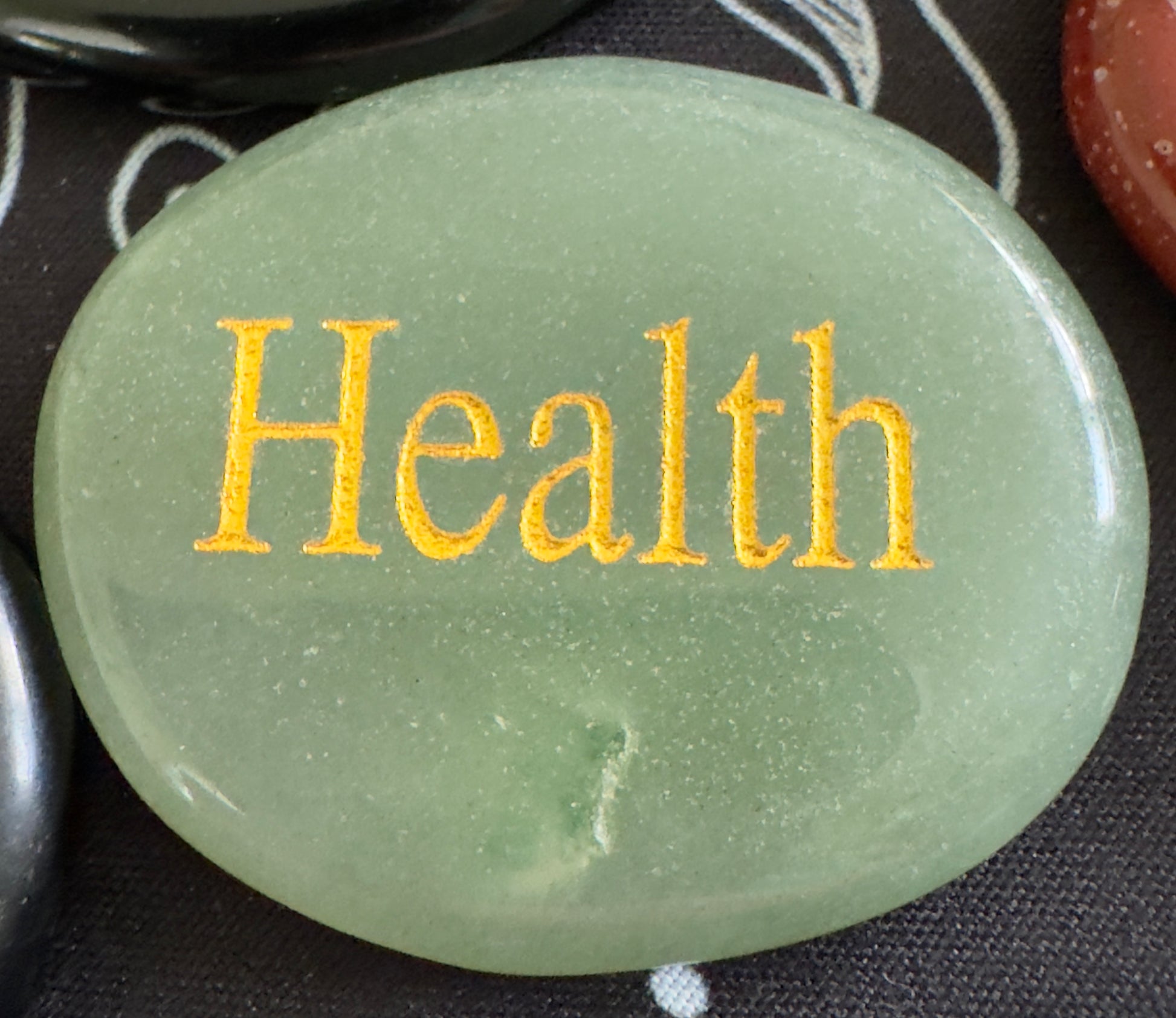 Close-up of a round, green gemstone with "Health" engraved in gold lettering.
