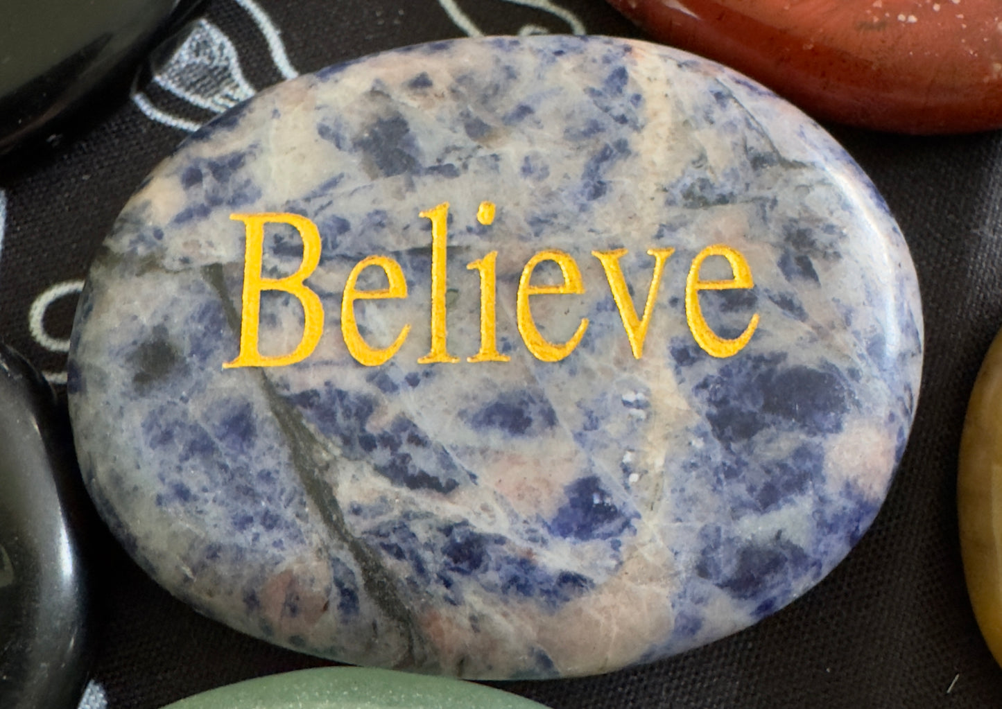 Oval sodalite stone with "Believe" inscription in gold.