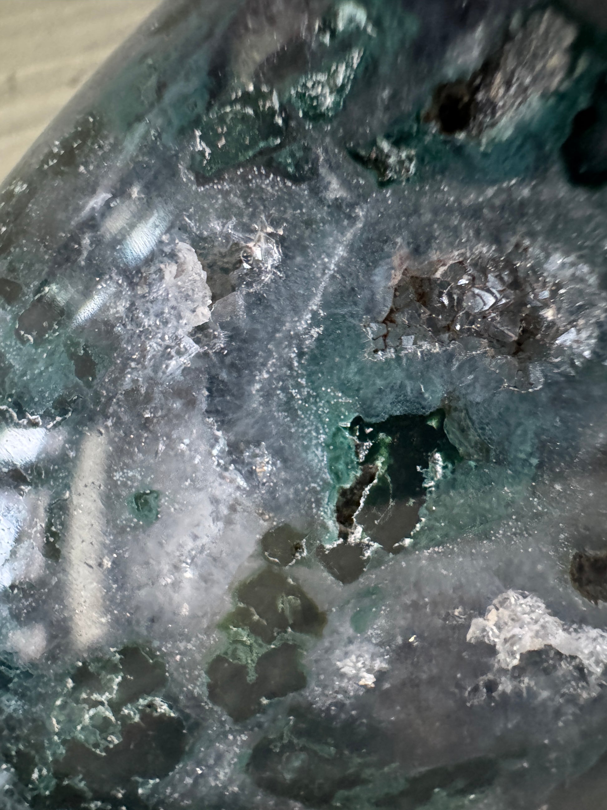 Close-up of a polished moss agate stone with green and gray inclusions.