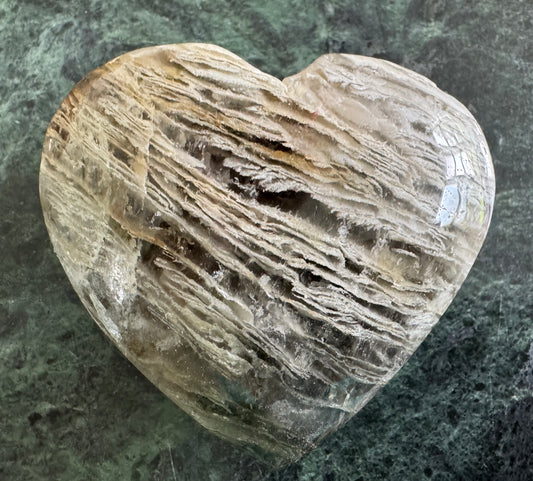 Heart-shaped crystal with layered patterns on a marbled green surface.
