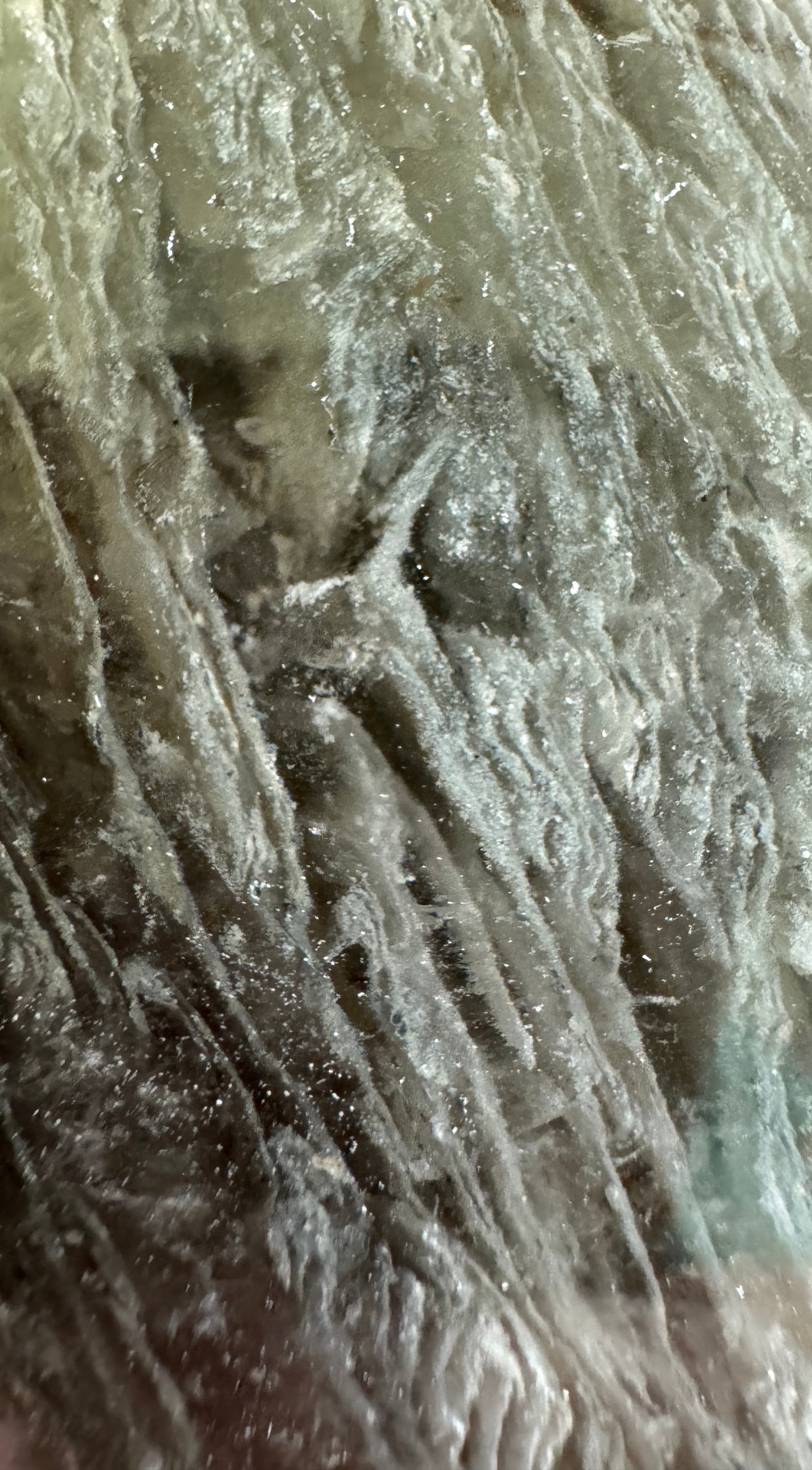 Close-up of a textured, translucent mineral surface with visible striations and sparkling inclusions.