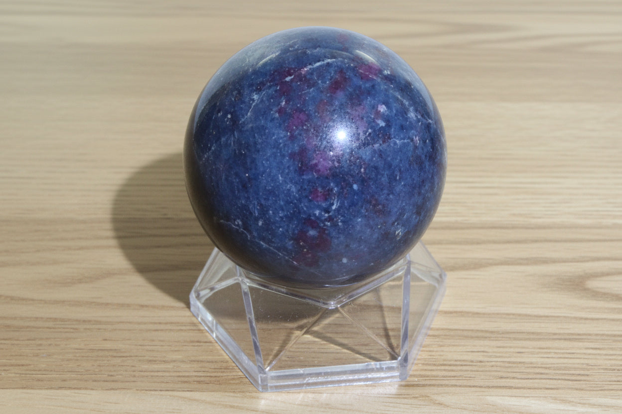 Ruby in Kyanite crystal sphere colors and red and blue, sphere is on a small stand sitting on a wood surface