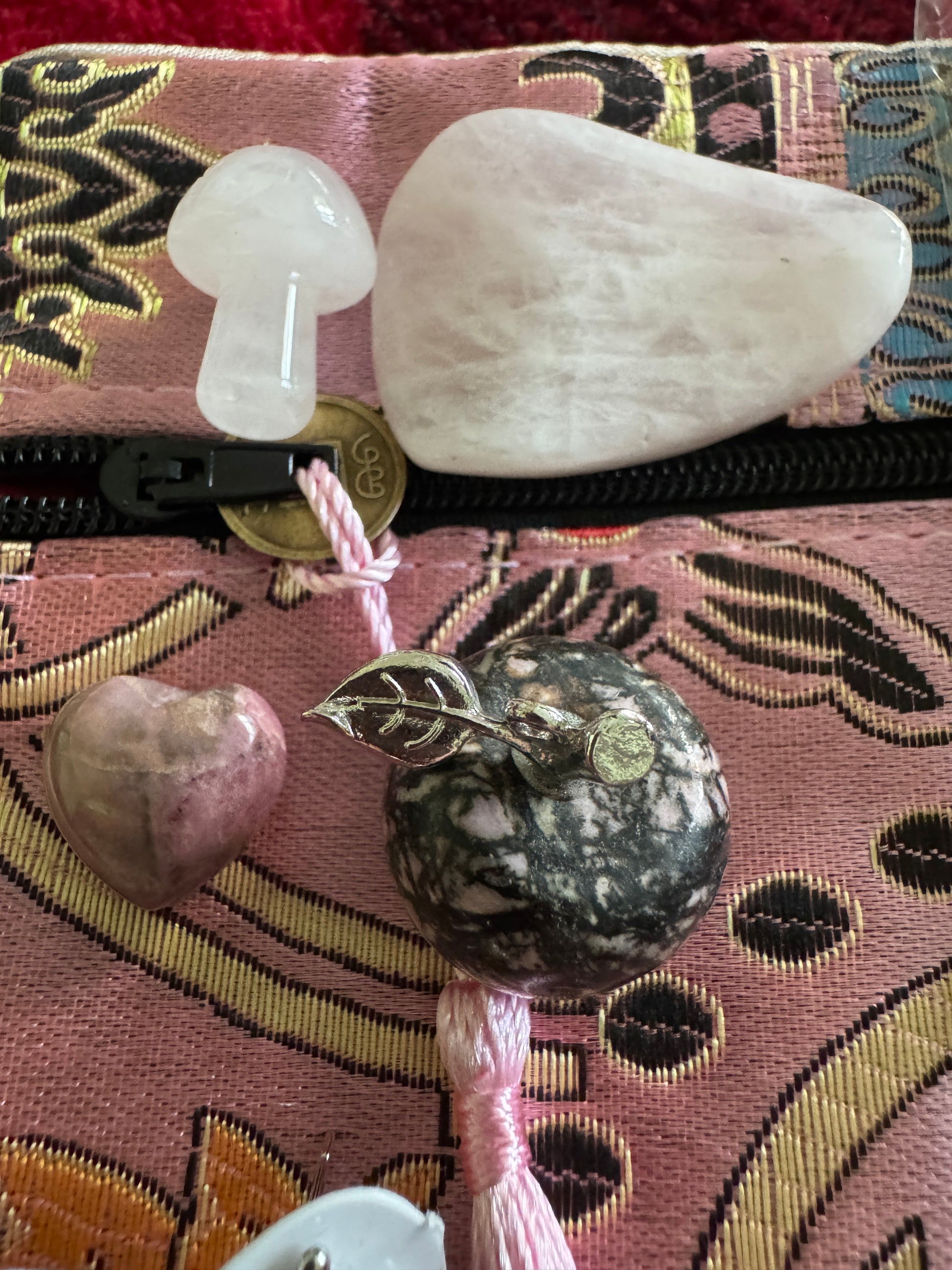 Close-up on a pink textured surface with a zipper, small mushroom, heart, and pebble with a silver leaf.