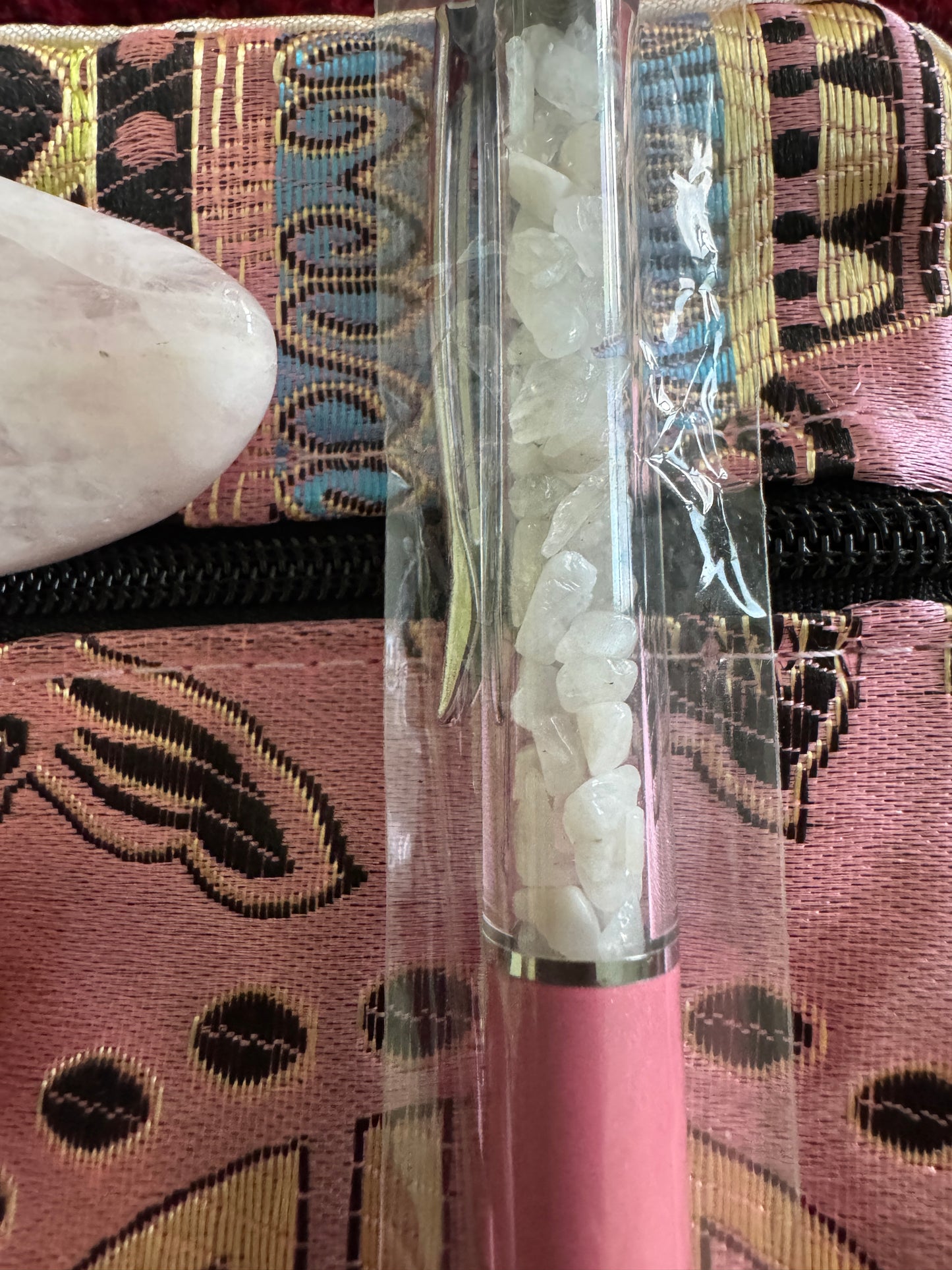 Pink patterned case, rose quartz stone, and a clear tube filled with small white crystals.
