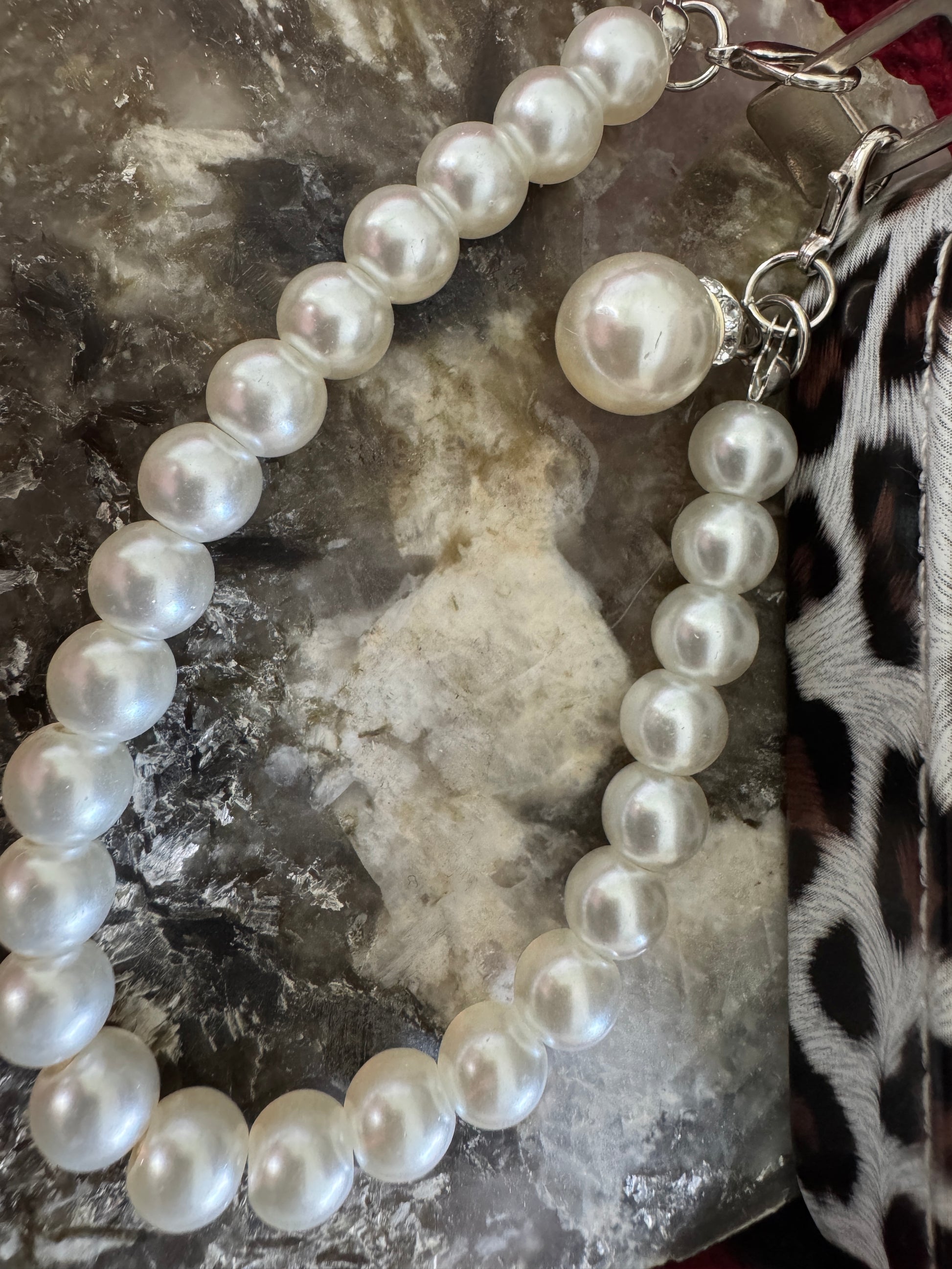 Pearl strap with silver clasps on marble stone and animal-print fabric.