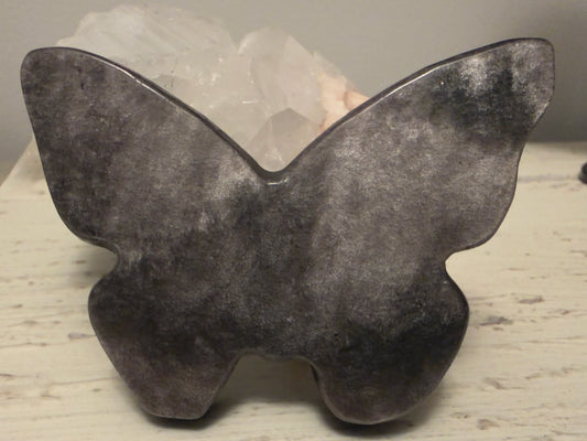 Golden Sheen Obsidian crystal carved butterfly leaning on a white rock. 

