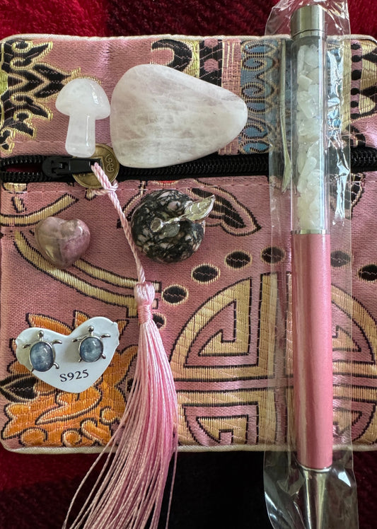 Assortment of crystals, jewelry, and a pen on a pink patterned pouch.
