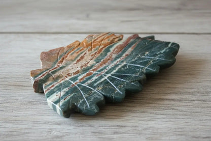 Green Jasper carving, hand tooled leaf shaped trinket dish Greens, rust colors on a table 
