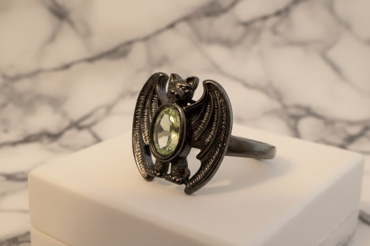 adjustable bat ring with a green peridot stone sitting on a white surface