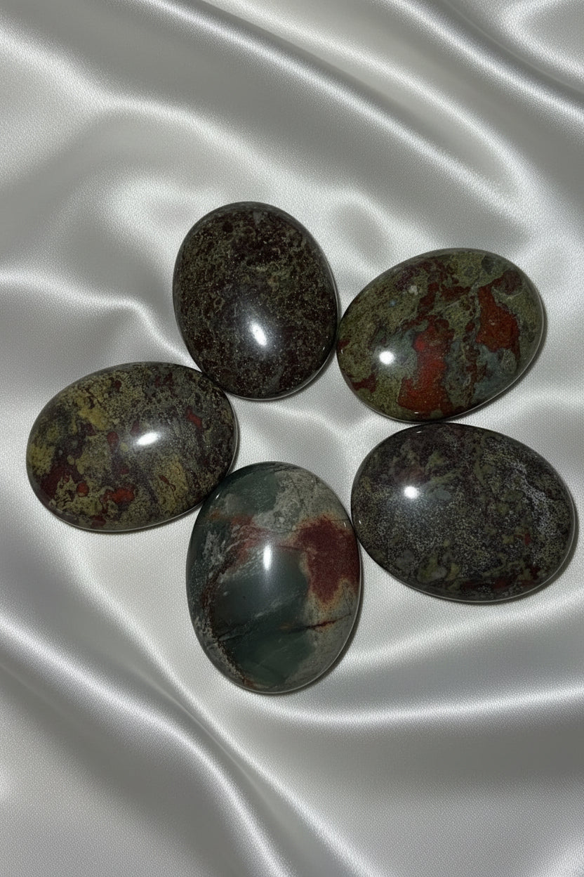 five dragonsblood polished palm stone crystals on an off white fabric