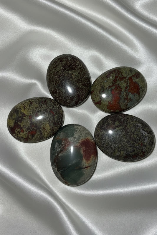 five dragonsblood polished palm stone crystals on an off white fabric