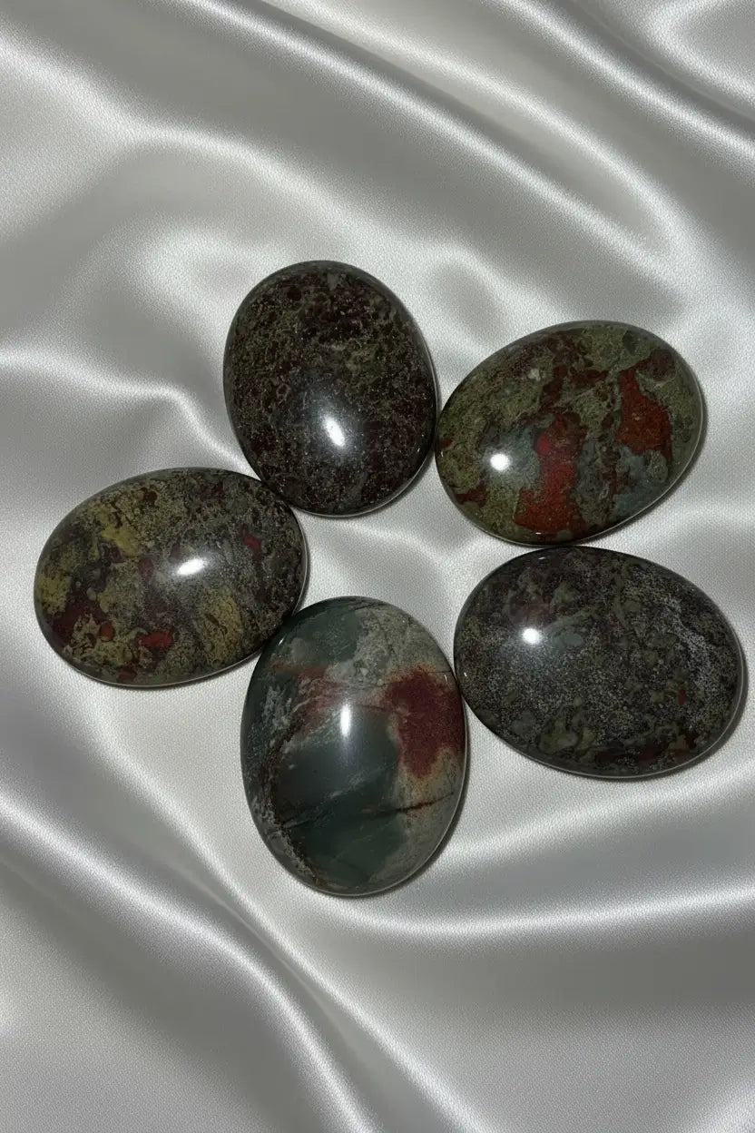 five dragonsblood polished palm stone crystals on an off white fabric