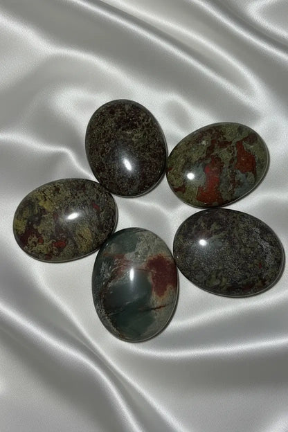 five dragonsblood polished palm stone crystals on an off white fabric
