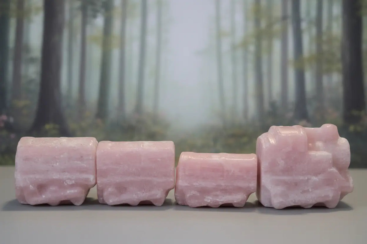 pink opal hand carved crystal four piece train set. muted forest behind 
