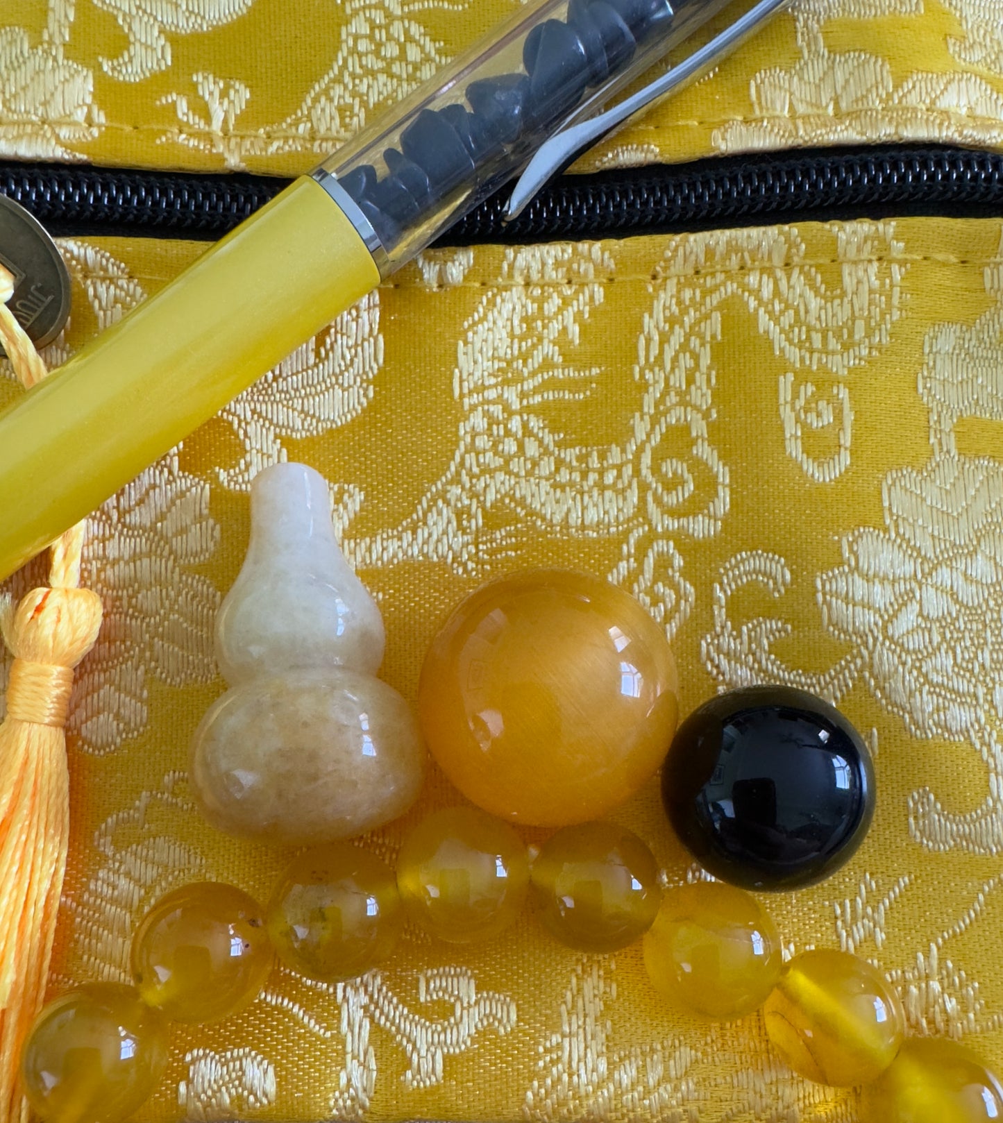 Assorted yellow stones and charms with yellow pen on gold patterned pouch.