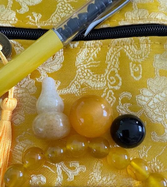 Assorted yellow stones and charms with yellow pen on gold patterned pouch.