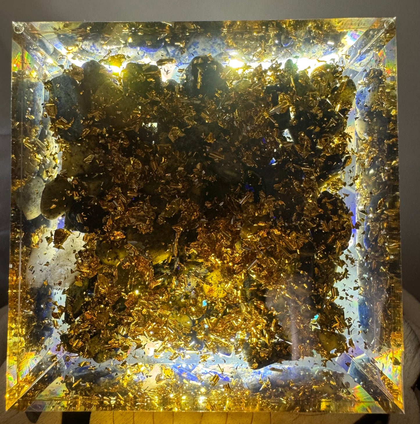 A transparent orgonite pyramid featuring a tightly wound copper spiral embedded in the center, with shimmering metal filings scattered throughout
