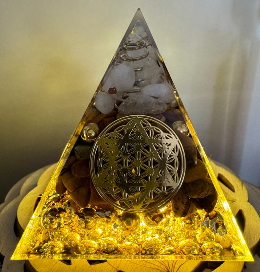 A pyramid-shaped orgonite with gold leaf, crystals, and a golden flower of life symbol.
