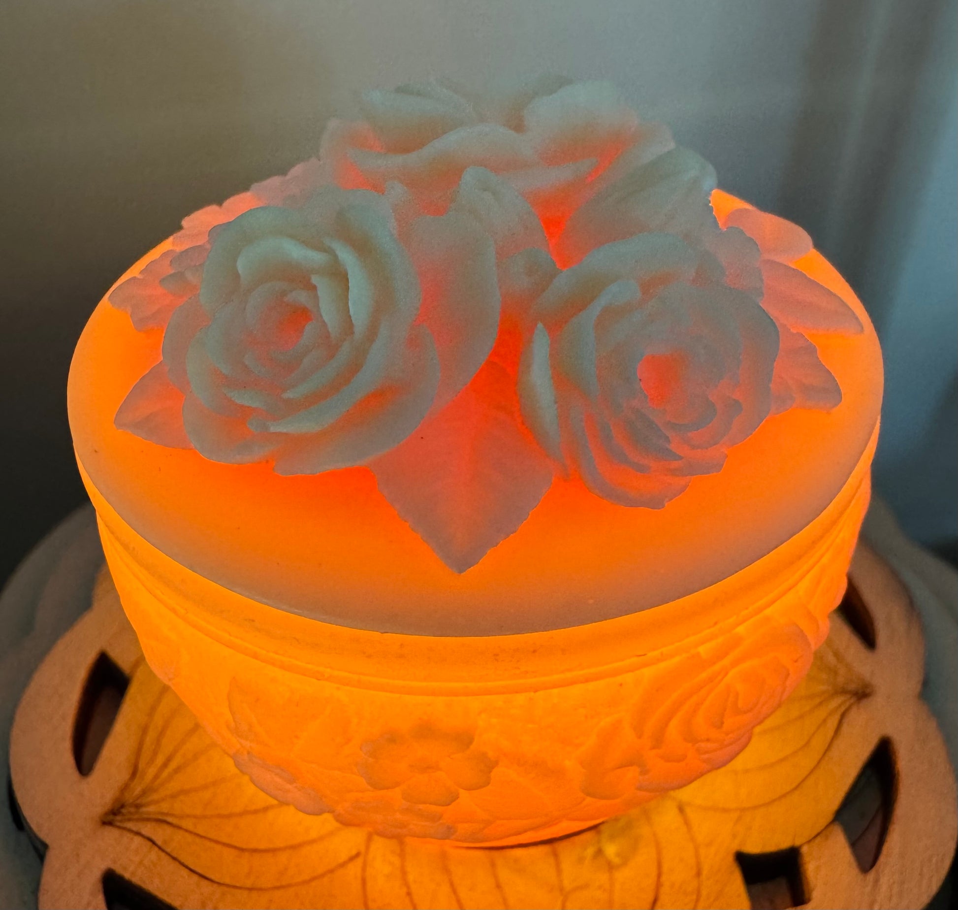 Illuminated, round, lidded container with white rose carvings.
