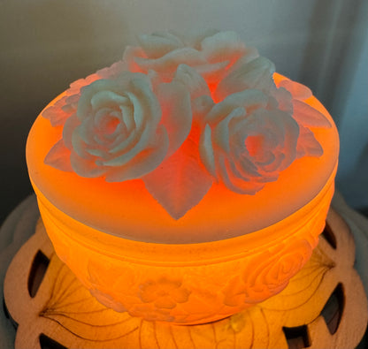 Illuminated, round, lidded container with white rose carvings.
