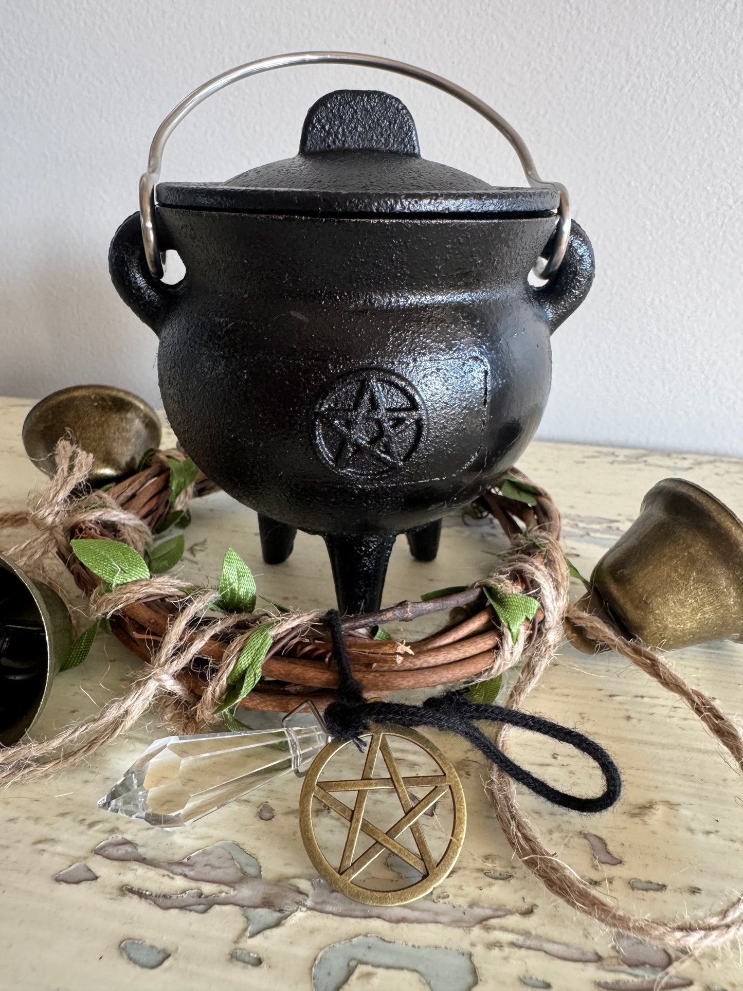  Triple moon pentacle black cast iron cauldron with lid, three legs, and metal handle, surrounded by rustic altar decor, crystal point, and gold pentagram ornament—perfect for witchcraft rituals, spellwork, and Wiccan altar supplies