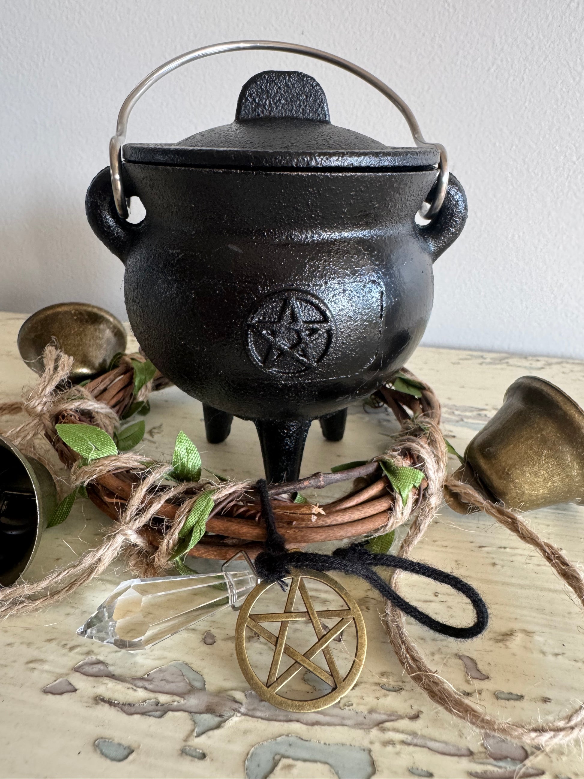  Triple moon pentacle black cast iron cauldron with lid, three legs, and metal handle, surrounded by rustic altar decor, crystal point, and gold pentagram ornament—perfect for witchcraft rituals, spellwork, and Wiccan altar supplies