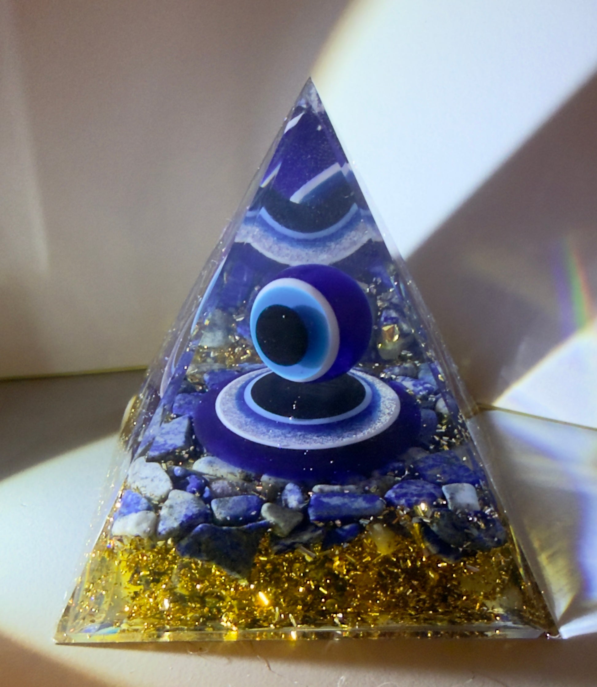 evil eye blue white black colors, sphere floating in orgonite pyramid with lapis lazuli crystals and copper chips, wire and bits