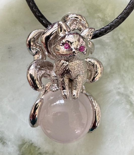 Silver fox pendant with pink eyes on a rose quartz ball, hanging from a black cord.
