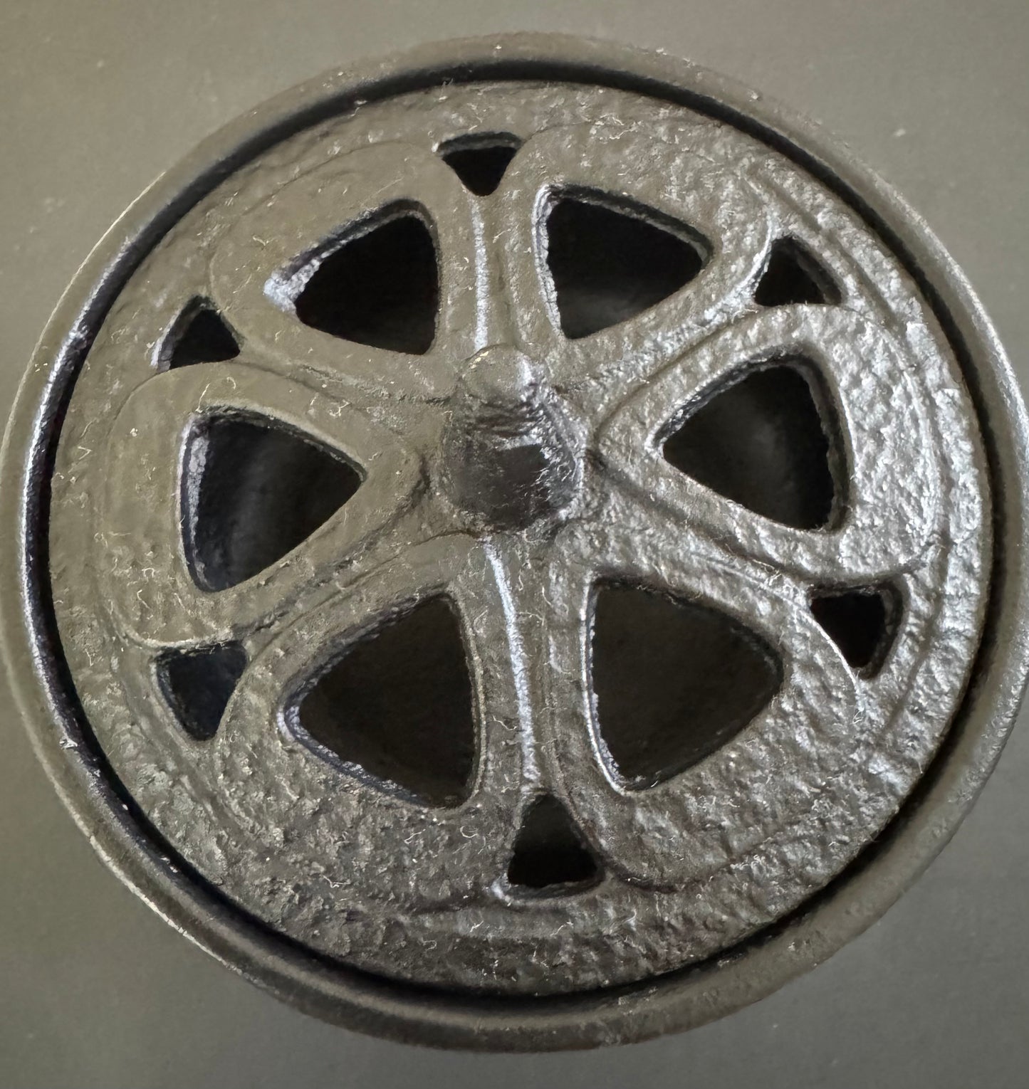 A small, black cast iron cauldron with a decorative pentacle design on the lid and three legs, close up overhead angle