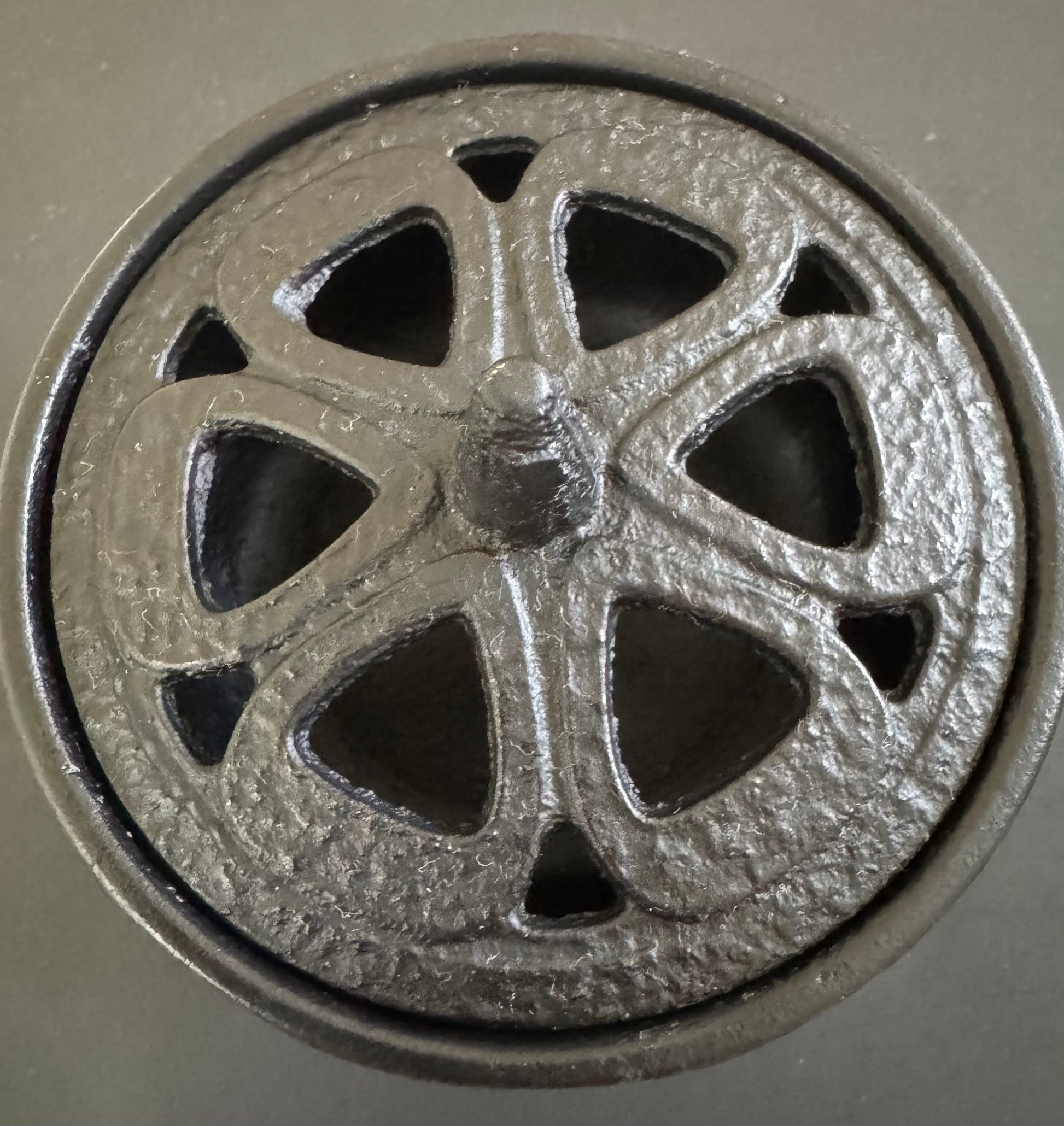A small, black cast iron cauldron with a decorative pentacle design on the lid and three legs, close up overhead angle