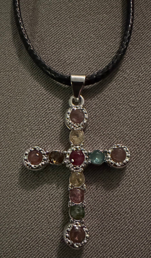 Close-up of a silver cross pendant with colorful stones on a black leather cord.
